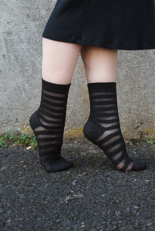 A person wearing Gossamer striped crew socks in black