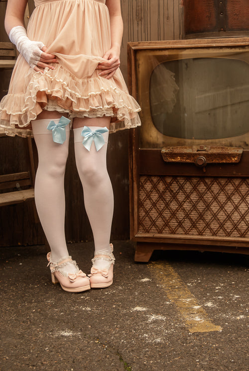 A person wearing opaque thigh high stockings in white with a light blue bow