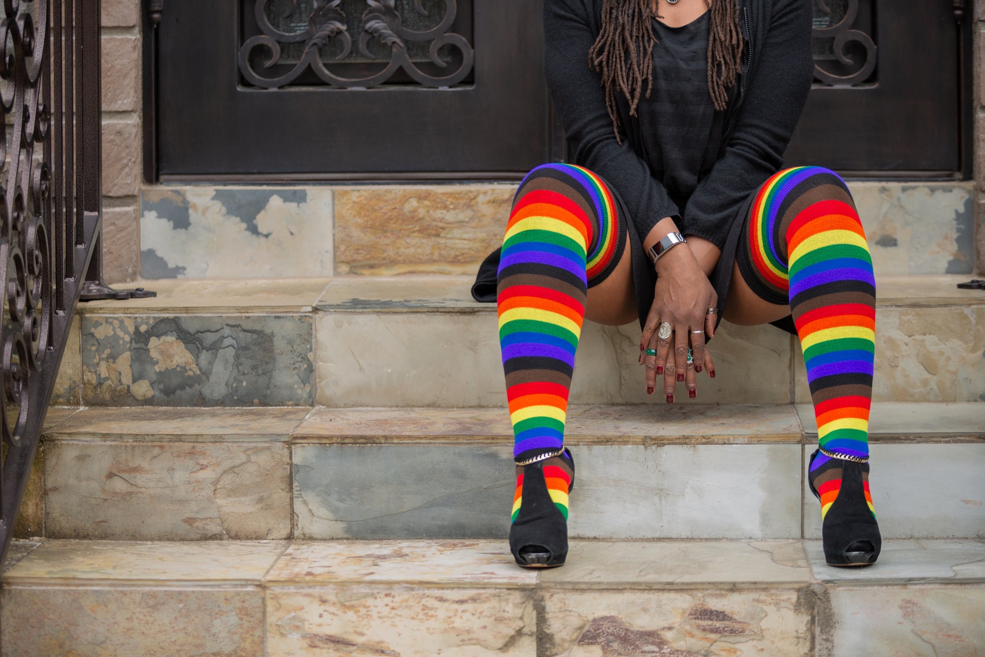 A model sitting on marble steps wearing Phiily Pride striped thigh high socks