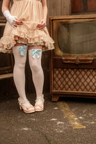 A person wearing opaque thigh high stockings in white with a light blue bow