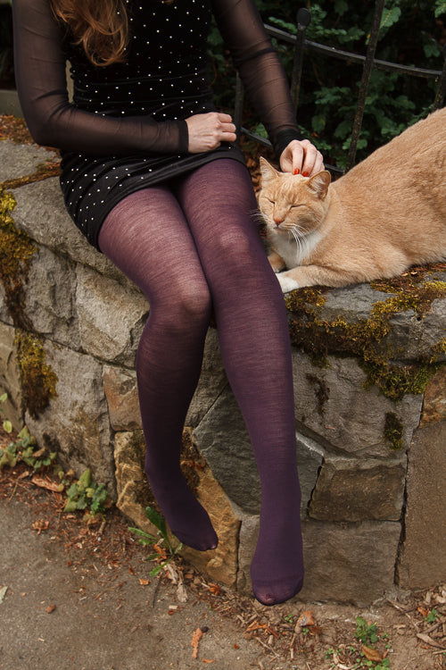A person wearing Jennifer Wool Tights in prune, with a cat next to them